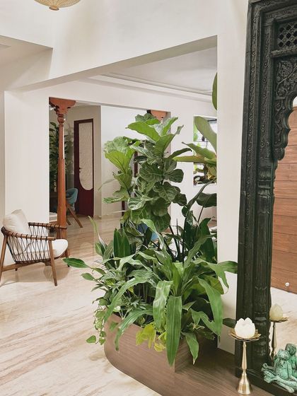 A carved wooden frame, reminiscent of an old doorway, is used here as a decorative mirror frame. It sits next to a lush indoor planter, blending traditional craft with the tropical aesthetic.