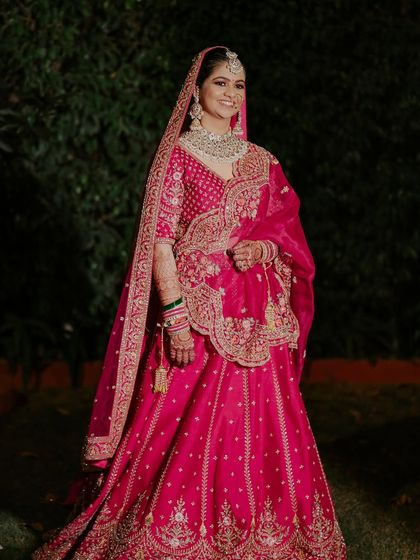A full-length shot of the bride in her magnificent pinkish-red lehenga. The makeup is balanced perfectly to complement the heavy outfit and jewelry.