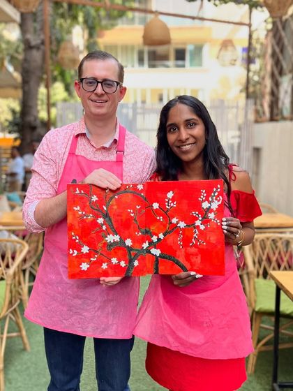 A couple holding their finished cherry blossom painting. A paint and sip session makes for a perfect and memorable date.