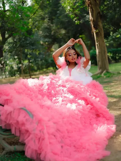 A whimsical and dramatic outdoor shoot featuring a model in an elaborate pink ruffled gown. The makeup is soft yet glamorous, with pink-toned eyeshadow and a defined liner to match the fantasy theme of the shoot.