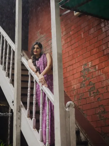 Using architecture to frame a portrait. The model poses on a white wooden staircase against a red brick wall, creating strong lines and a visually interesting composition for this full-length saree shot.