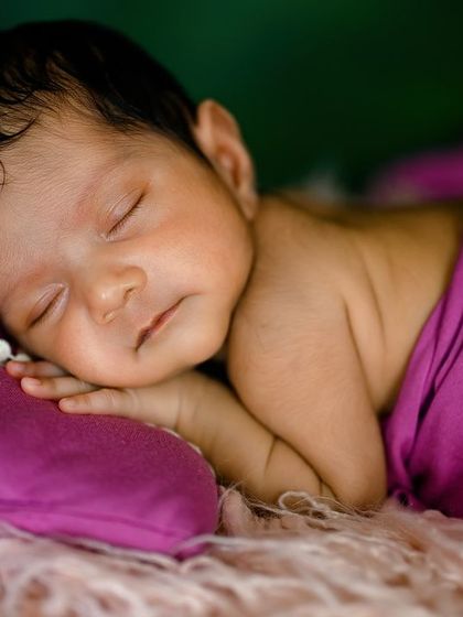A close-up shot focusing on the serene face of a sleeping newborn, wrapped in a beautiful magenta fabric.