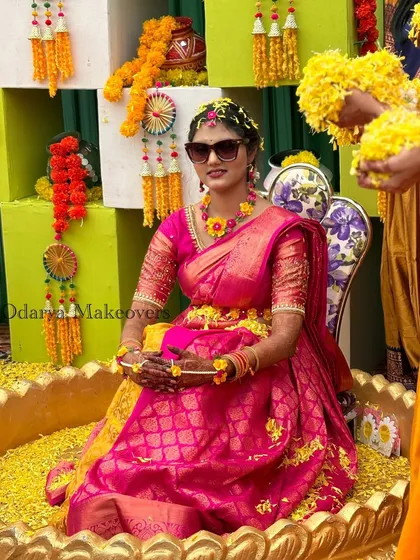 A full view of the bride during her flower Haldi ceremony. The vibrant pink and yellow of her outfit and the decor create a stunning visual.