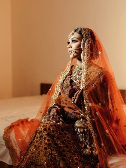 A side profile of the bride seated, the warm lighting highlighting the intricate details of her bridal outfit and jewelry.