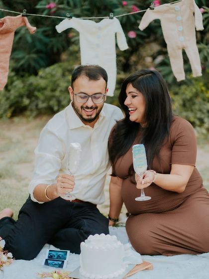 The big reveal. This photo captures the couple's joyful reaction during their outdoor gender reveal, with a line of baby clothes creating a charming backdrop.