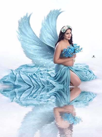 A magical portrait featuring a client in a turquoise wrap, holding matching flowers, with digitally added angel wings. The water reflection completes this ethereal and heavenly scene.