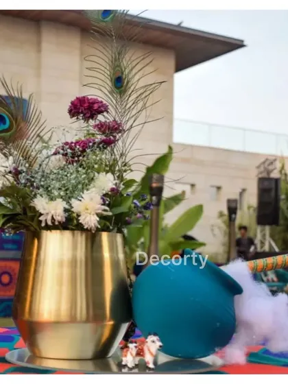 A beautiful centerpiece for the Vrindavan theme, featuring a brass vase, peacock feathers, and a pot with dry ice for a mystical smoke effect.