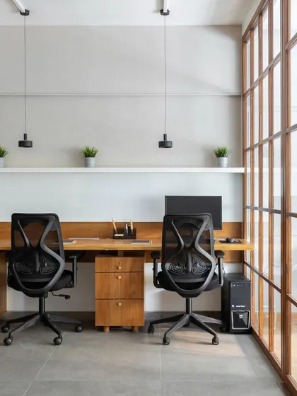 A shared workstation area designed with simplicity and function in mind. The long wooden desk, minimal pendant lights, and ergonomic chairs create a clean and productive workspace.