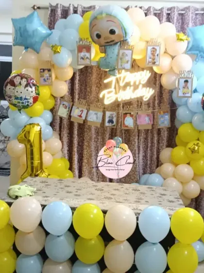 A sweet Cocomelon themed first birthday setup for a home party, with a pastel balloon arch and a shimmer curtain backdrop.
