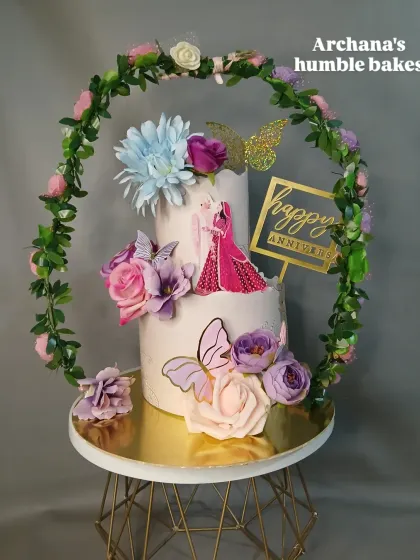 A two-tiered anniversary cake framed by a beautiful floral hoop. The purple and pink flowers create a romantic and whimsical feel.