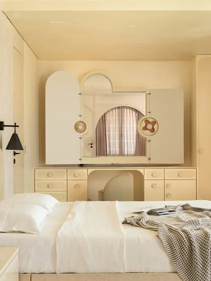 The master suite in the 'Soft Serve' project is enveloped in a timeless taupe. The custom bed and vanity feature abstract patterns in Movingue White veneer, with scalloped motifs framing the bay window.