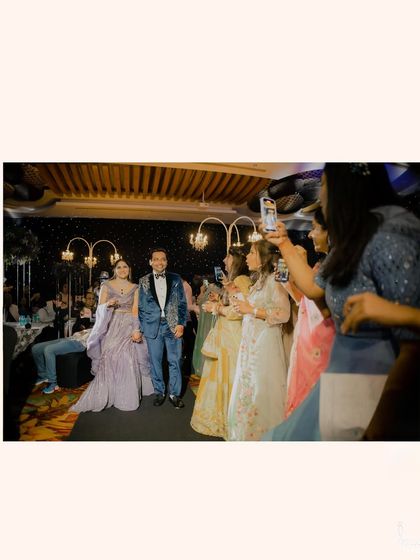 The couple's grand entrance at their Sangeet, with guests capturing the moment on their phones. A modern and fun celebration.