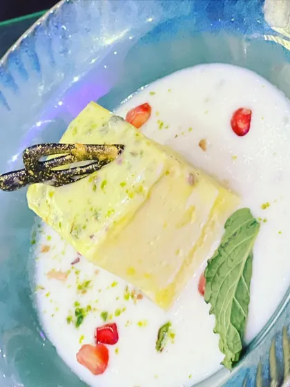 A modern take on a traditional Indian dessert. This pistachio kulfi is served in a contemporary bowl with rabri and pomegranate seeds, blending classic flavors with stylish presentation.