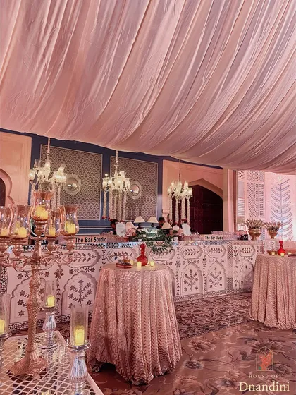 The bar area, with a custom-made front featuring traditional Rajasthani motifs. The space is softened with fabric draping and illuminated by elegant chandeliers.