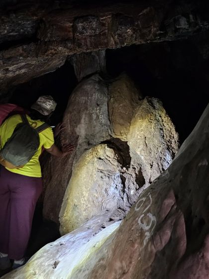 A trekker examining the unique rock formations inside a cave with the help of a torch.