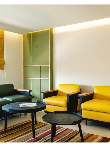 The suite's living area continues the green and yellow color scheme, with contemporary furniture and a vibrant, multi-colored rug. The space is designed to be both stylish and comfortable for guests.