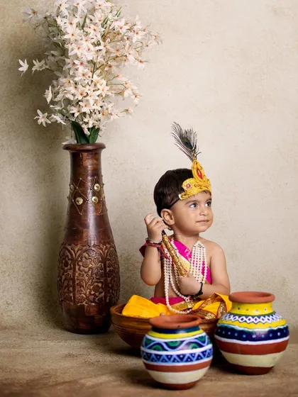 This photo shows a more elaborate setup with a little Krishna surrounded by traditional pots and a vase of flowers, creating a serene and artistic composition.