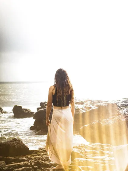 A dreamy, ethereal shot of a woman looking out at the sea. I used a lens flare effect to create golden rays of light, adding a magical and serene quality to this beach portrait.