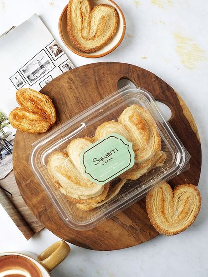 A box of my freshly baked Palmiers, sitting on a wooden board. These crisp, golden biscuits are baked to perfection, never fried, making them a satisfying and wholesome treat.