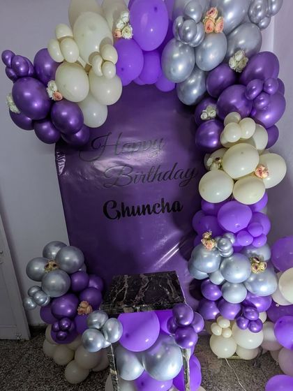 This setup includes a matching pedestal for the cake, fully integrated into the purple and silver balloon decoration.