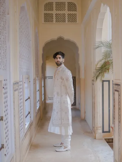 A solo portrait of the groom in a sunlit palace corridor. The clean lines of the architecture and the soft light highlight the quiet elegance of his traditional attire.