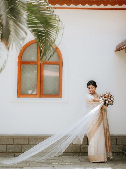 A full-length portrait of the bride, her long veil trailing behind her, framed by a palm frond.