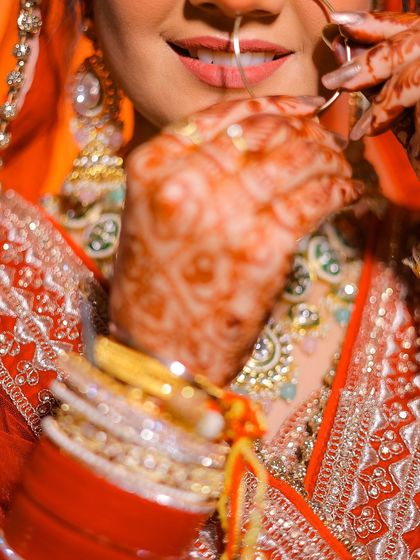 An artistic close-up on the bride's smile and nath, with the hennaed hand adding texture.