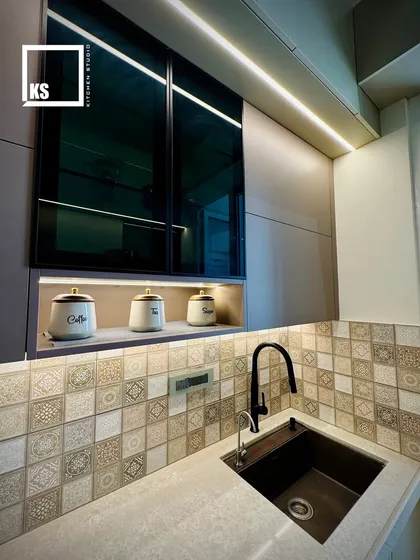 The sink area features a modern black faucet that complements the dark accents in the cabinetry and backsplash. The under-mount sink provides a seamless and easy-to-clean counter surface.