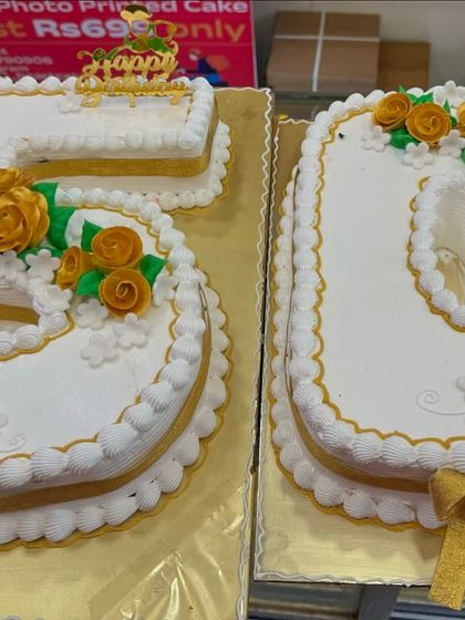 A grand number cake for a 50th birthday celebration. The numbers '5' and '0' are shaped into cakes and elegantly decorated with golden-yellow roses and ribbons.
