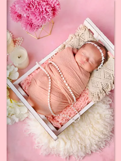 A lovely pink-themed setup with a newborn sleeping in a miniature white bed. The pearls, candles, and flowers create a soft, romantic, and girly atmosphere.