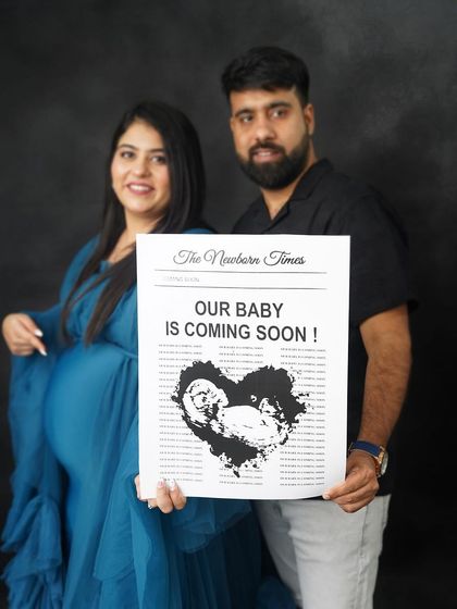 A creative pregnancy announcement. The couple holds a custom "Newborn Times" newspaper prop, a unique and fun way to share their exciting news.