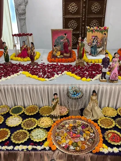 A grand `rukhwat` table featuring multiple doll vignettes, a large spread of `namkeen` on a blue tablecloth, and a central `chappan bhog` platter.