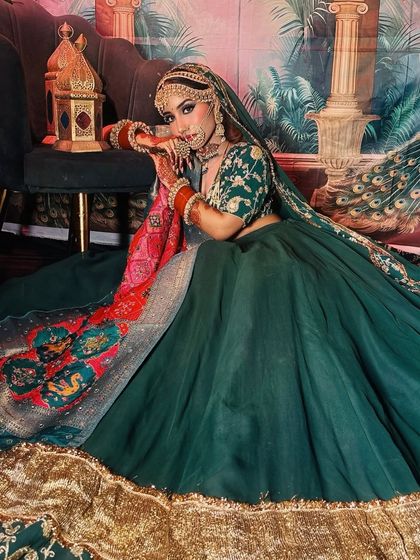 A full shot of the bride in the green lehenga, seated in a regal setting.