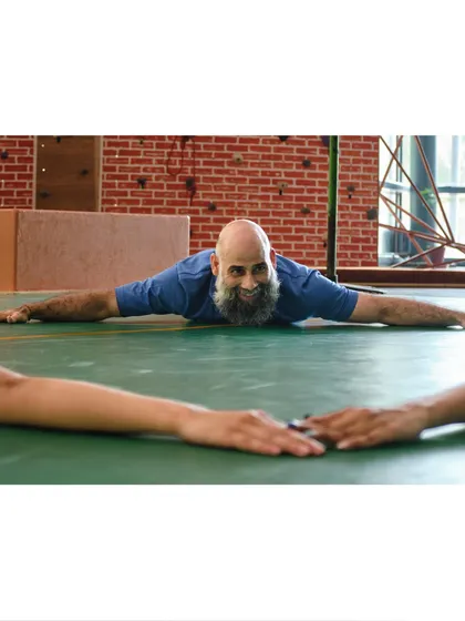 Our instructor smiles while demonstrating a deep floor stretch, showcasing the flexibility and positive energy he brings to every class.