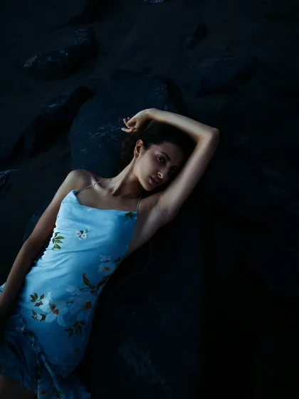 A close-up portrait from the same series, focusing on the model's gentle expression and the soft, floral-print dress against the dark, textured rocks.