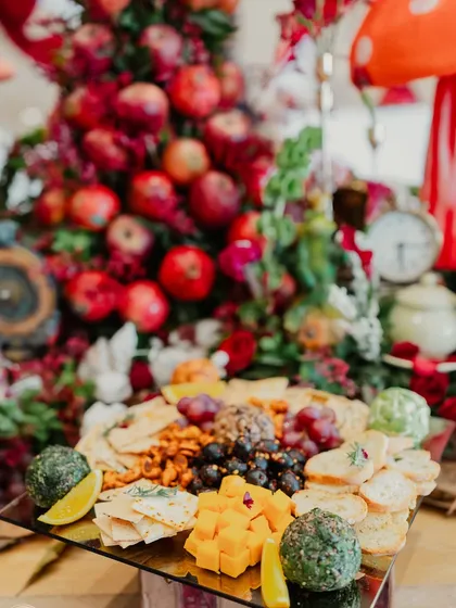 A whimsical Alice in Wonderland themed grazing table for a 6-month birthday celebration, featuring a cheese board set against a tower of red apples.