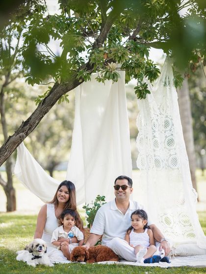 A classic family portrait with a natural, relaxed feel. The white outfits create a timeless look against the green backdrop of the park.