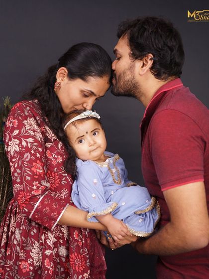 An intimate and loving family portrait. The parents' gentle kisses on their baby's head create a circle of love and protection. This is a perfect example of a tender family moment.