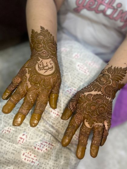 A lovely design featuring a name in Arabic script inside a central circle, surrounded by floral patterns. The other hand has a matching floral design.
