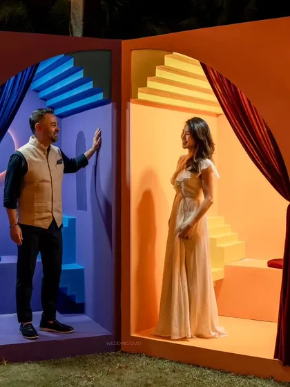 Our sangeet photo booth was designed as two separate, color-blocked worlds. The couple poses in the contrasting blue and orange spaces, creating a surreal and artistic portrait.
