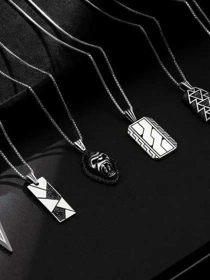 A moody group shot of men's necklaces, laid out on a dark, textured surface to create a sophisticated and masculine feel.