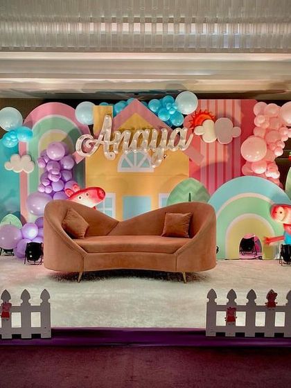 A perfect Peppa Pig stage setup for a third birthday, featuring a cute house backdrop, character cutouts of Peppa and George, and a comfy sofa for the birthday star.