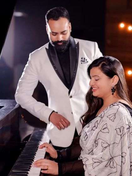 A classic portrait of a couple at the piano. The man stands behind the woman as she plays, creating a scene of shared harmony and elegance for their pre-wedding album.