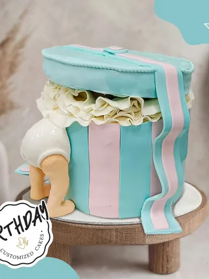 Peek-a-boo! This adorable baby-themed cake features a baby bottom diving into a gift box, making it a fun and whimsical choice for a first birthday or baby shower.
