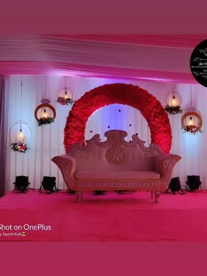 A modern and chic engagement or reception stage with a striking red floral crescent moon backdrop. The design is complemented by hanging decorative hoops with lights, all set on a plush pink carpeted stage.
