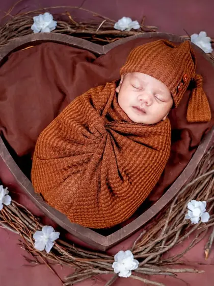 A baby snuggled warmly inside a heart-shaped wooden nest, showing how I use props to create a feeling of love and security.