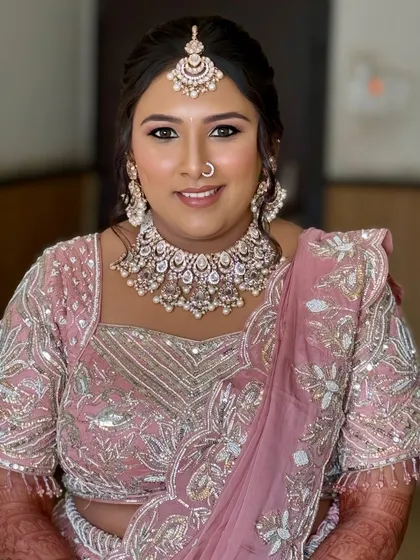 A full view of the bride in her pastel pink lehenga. The makeup is designed to complement the soft, dreamy vibe of the outfit.