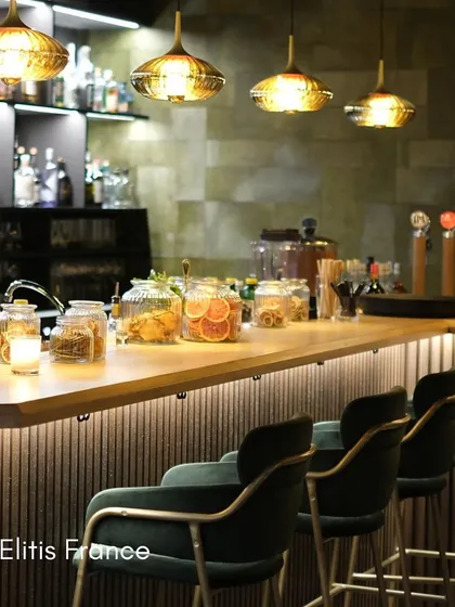 In this bar setting, a textured wallcovering from Élitis France adds a layer of timeless elegance. The subtle pattern complements the warm lighting and rich materials, contributing to an atmosphere of pure opulence.