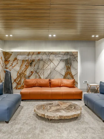 This lounge area features a striking backlit onyx wall, providing a warm, ambient glow. The space is furnished with modern blue and orange leather sofas and a rustic live-edge wood coffee table.