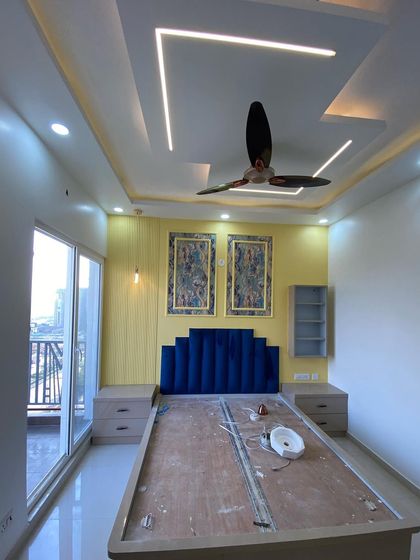 A wide view of the master bedroom, showing the bed, side tables, and the beautiful false ceiling with profile lighting.